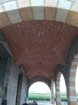 Techo abovedado de ladrillo de un porche, con arcos de piedra. El techo es de color marrón rojizo, con arcos blancos y tostados.