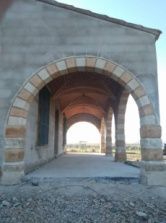 Pasarela arqueada de piedra sobre un edificio, que conduce a un exterior luminoso, de piedra beige y tostada.