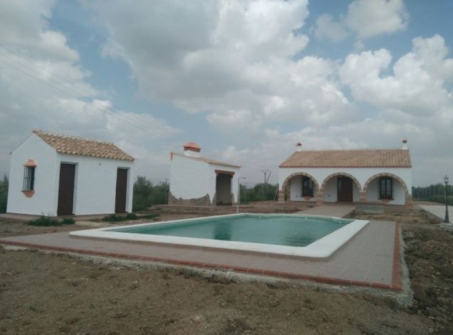 Edificios blancos con techos de tejas marrones, piscina y cielo nublado.