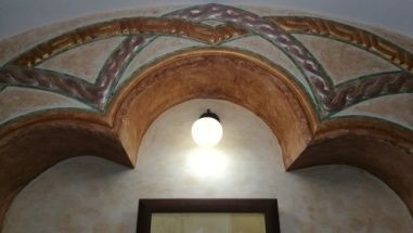 Puerta arqueada con pintura decorativa encima, una sola bombilla y una puerta con marco oscuro debajo.