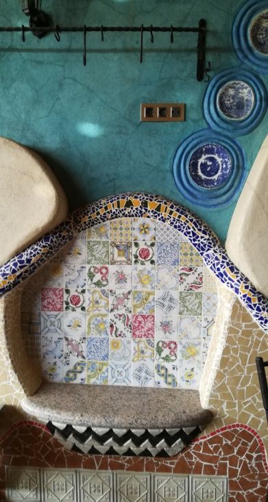 Azulejos ornamentados en una hornacina curva, pared turquesa, platos decorativos y una barra de metal oscuro con ganchos.