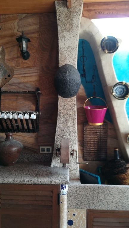 Encimera de cocina con paneles de madera, detalles de piedra y varios objetos, entre ellos una maceta y una cesta colgantes.