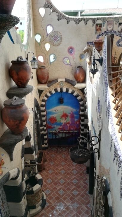 Pasillo arqueado con macetas de cerámica, mosaicos y obras de arte coloridas.