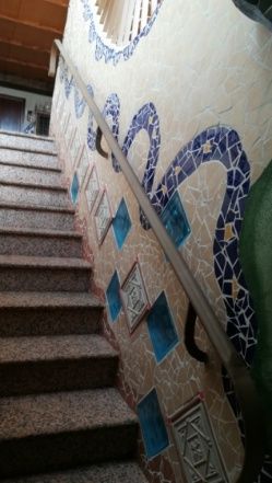 Escalera con escalones de piedra texturizada, pared revestida de mosaicos con diseños azules y blancos y pasamanos de madera.