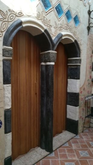 Dos puertas de madera en aberturas arqueadas con columnas decorativas en blanco y negro y pared de estuco circundante.