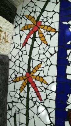 Arte de pared en mosaico con dos libélulas y enredaderas verdes sobre fondo blanco.