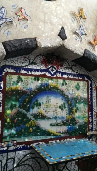 Obra de mosaico con una escena de paisaje central, rodeada de azulejos brillantes y decoraciones de mariposas.