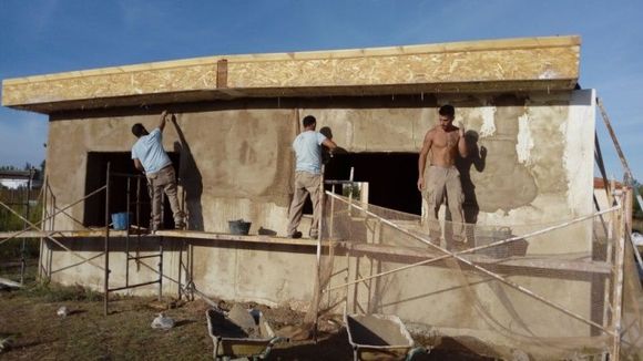 Obreros enyesando el exterior de un pequeño edificio. Andamios rodean la estructura.