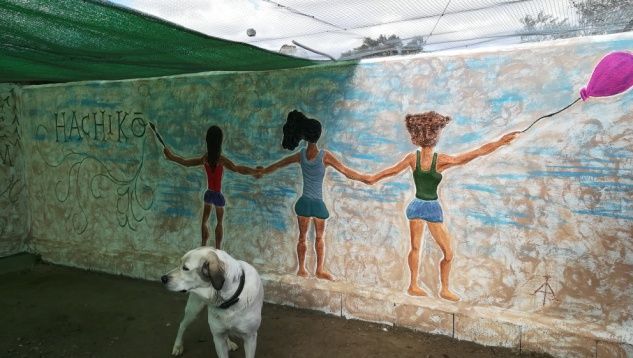 Perro frente a un mural de tres figuras tomadas de la mano, una de ellas con un globo rosa.