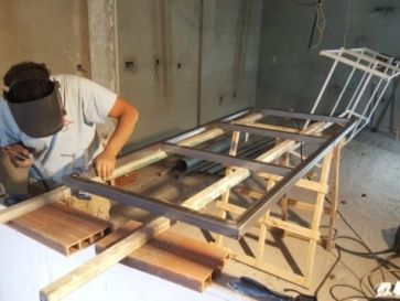 Persona soldando una estructura metálica sobre un soporte de madera en un entorno de construcción.