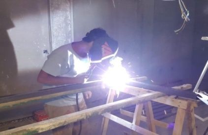 Persona soldando metal en un taller, con máscara de soldar, salen chispas.