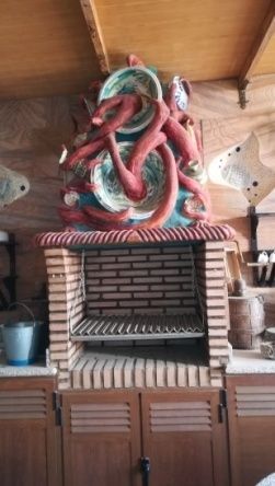 Parrilla de barbacoa de ladrillo con escultura de pulpo rojo en la parte superior, gabinetes de madera.