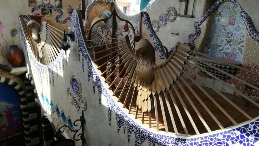 Banco de mosaico con detalles de madera en forma de abanico. Azulejos de cerámica decorativos y un soleado entorno exterior.