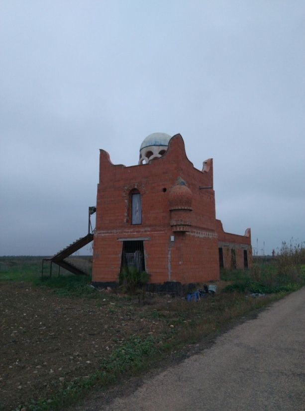 Edificio de ladrillo rojo con cúpula, en un campo, bajo un cielo nublado.