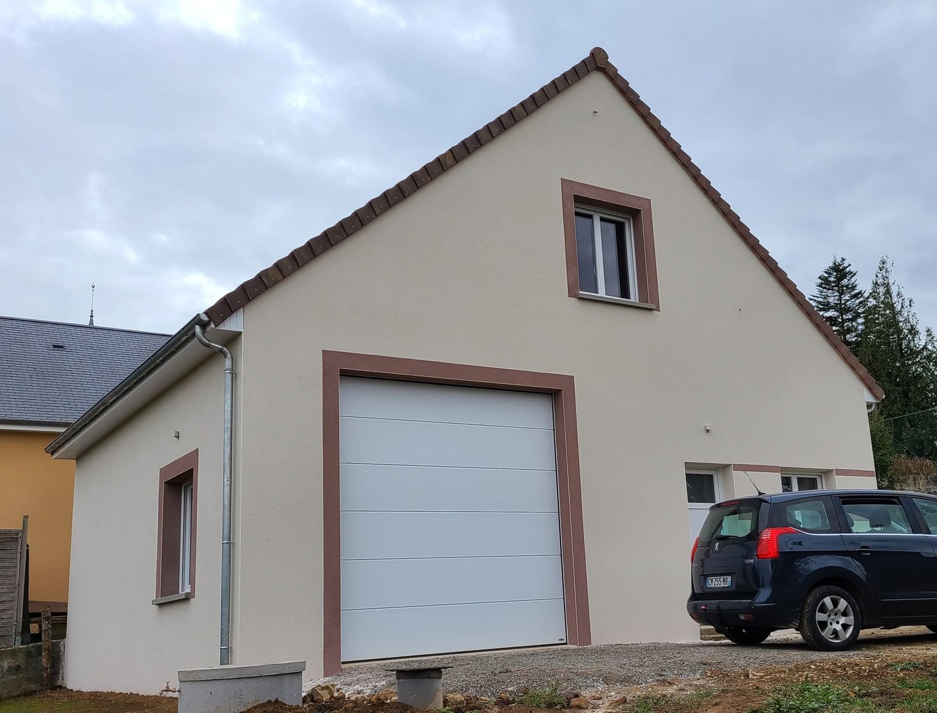 Fondations en béton en construction avec treillis d'armature, terre au premier plan, maisons et arbres en arrière-plan.