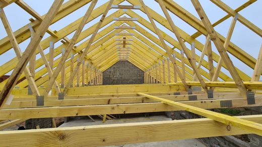 Vue intérieure d'une charpente de toit en bois en construction, avec des poutres en bois jaune et le ciel ouvert au-dessus.