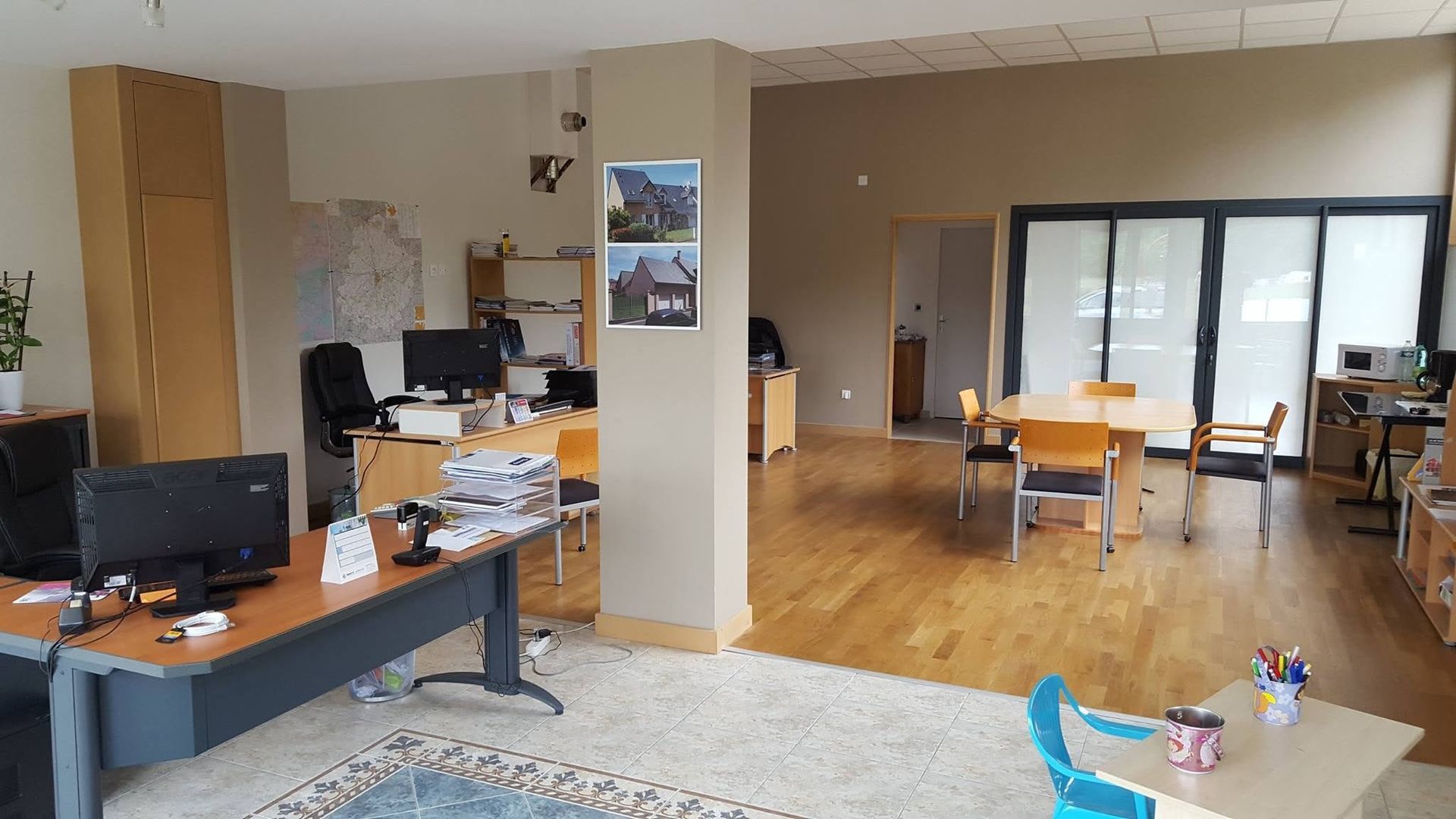 Bureau ouvert avec bureaux, ordinateurs, parquet et une petite table à manger près de portes coulissantes en verre.