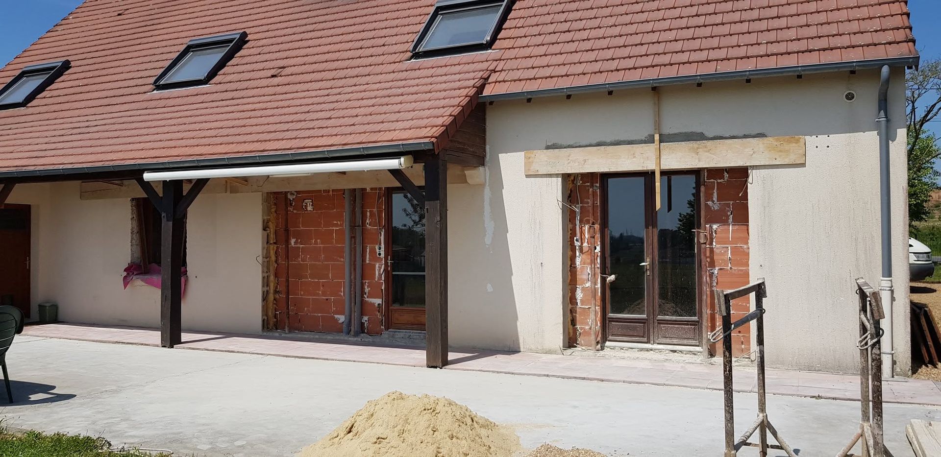 Rangée de maisons inachevées aux toits rouges, portes ouvertes et matériaux de construction à l'extérieur.