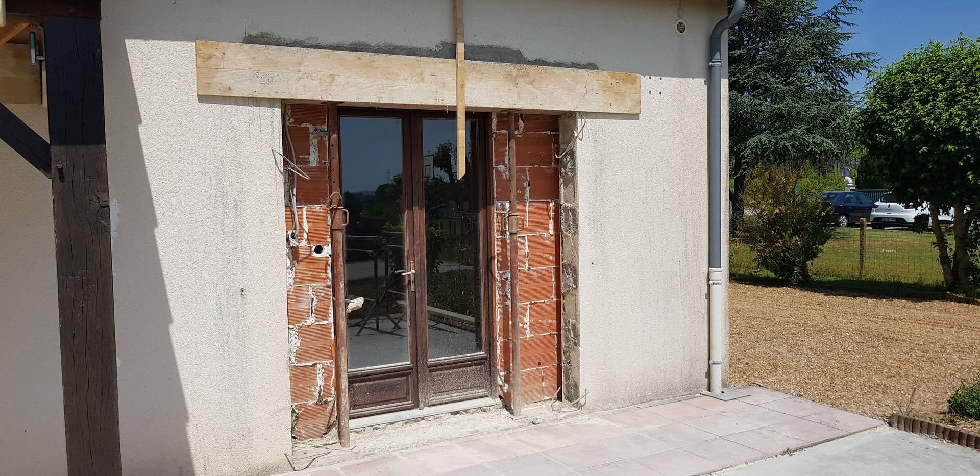 Porte d'entrée en briques avec porte vitrée et volets sur un bâtiment en stuc, à côté d'une allée et d'une pelouse.