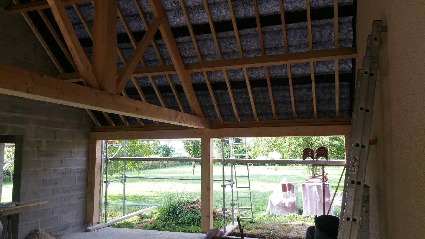 Intérieur d'une pièce inachevée avec poutres apparentes, mur ouvert et échelle appuyée contre le mur droit.