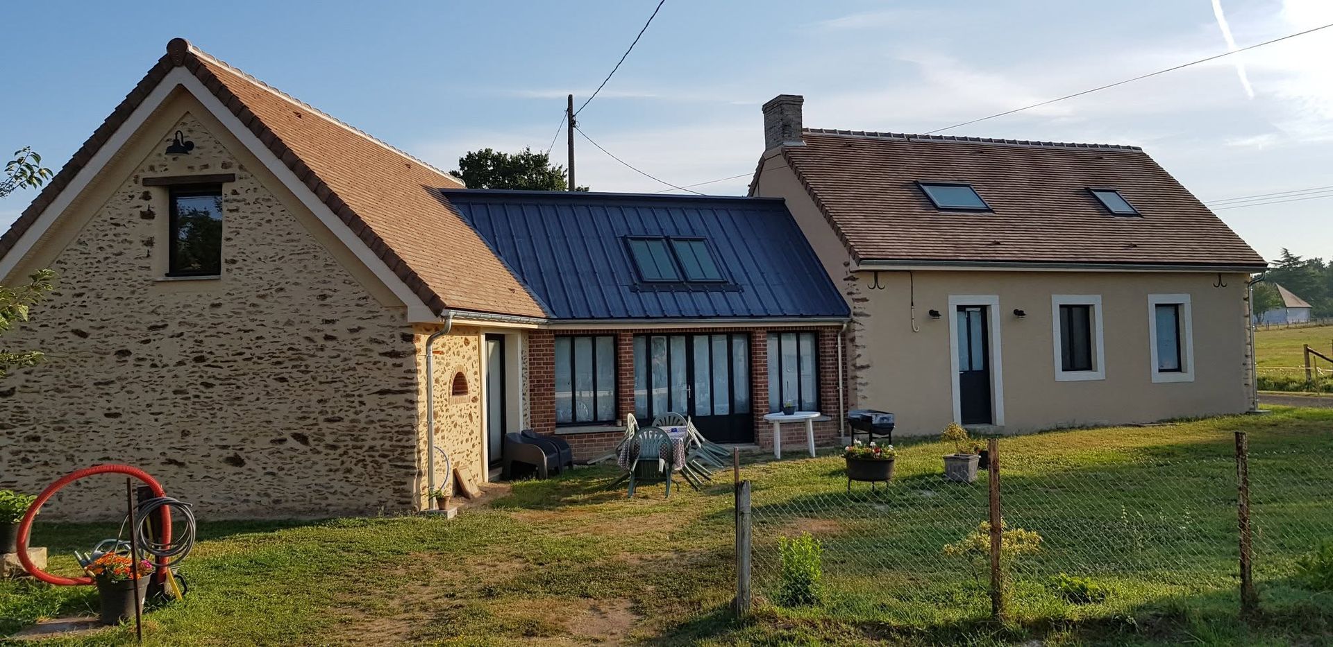 Maison en pierre et beige avec un toit en pente et des panneaux solaires, vue depuis une cour gazonnée par une journée ensoleillée.