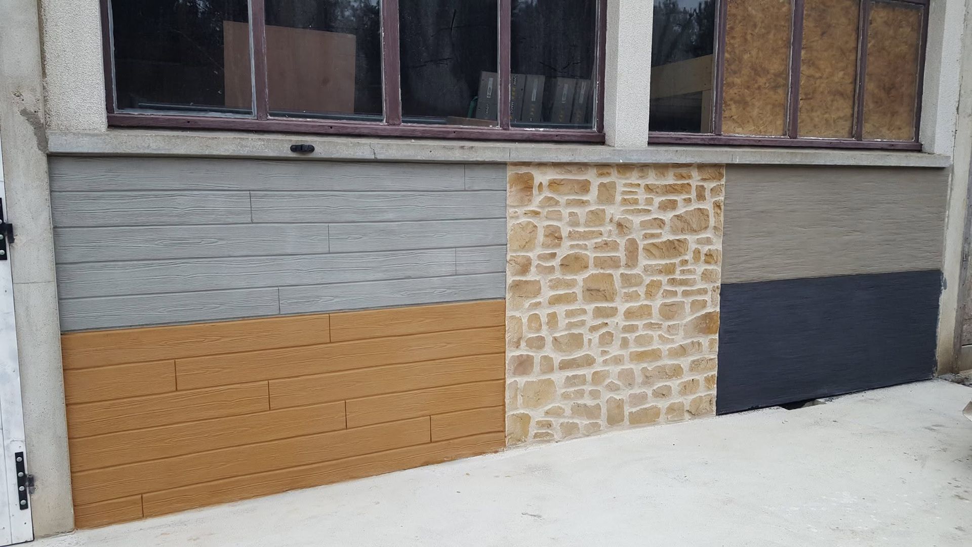 Mur extérieur avec un mélange de briques, de pierres et de panneaux sombres sous les fenêtres.