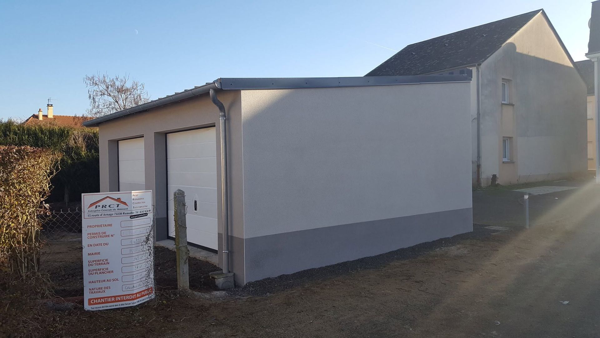 Bâtiment blanc à base grise, porche latéral et panneau d'affichage extérieur au soleil