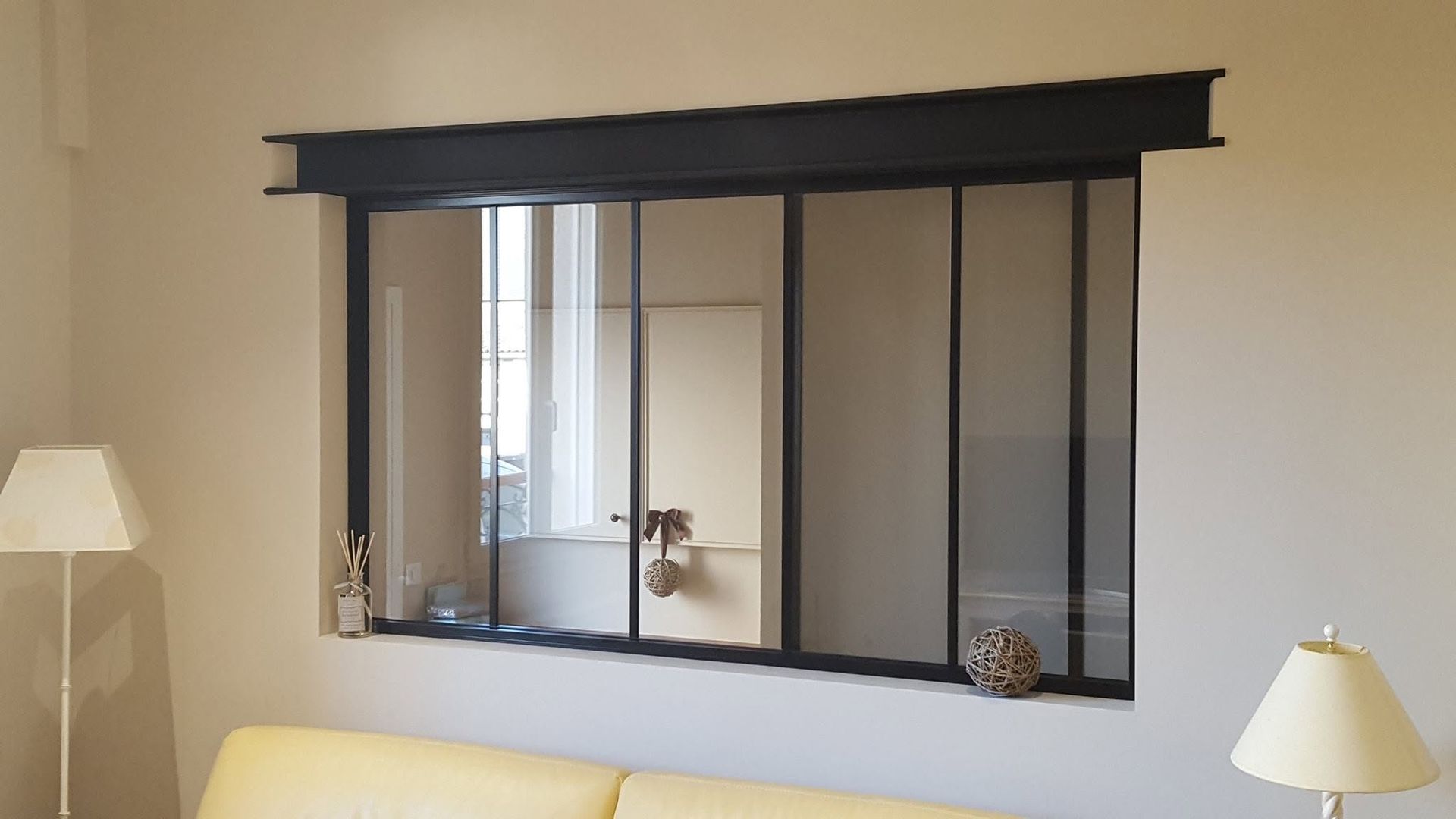 Mur du salon avec un grand miroir à cadre noir au-dessus d'un canapé beige et de deux lampes.