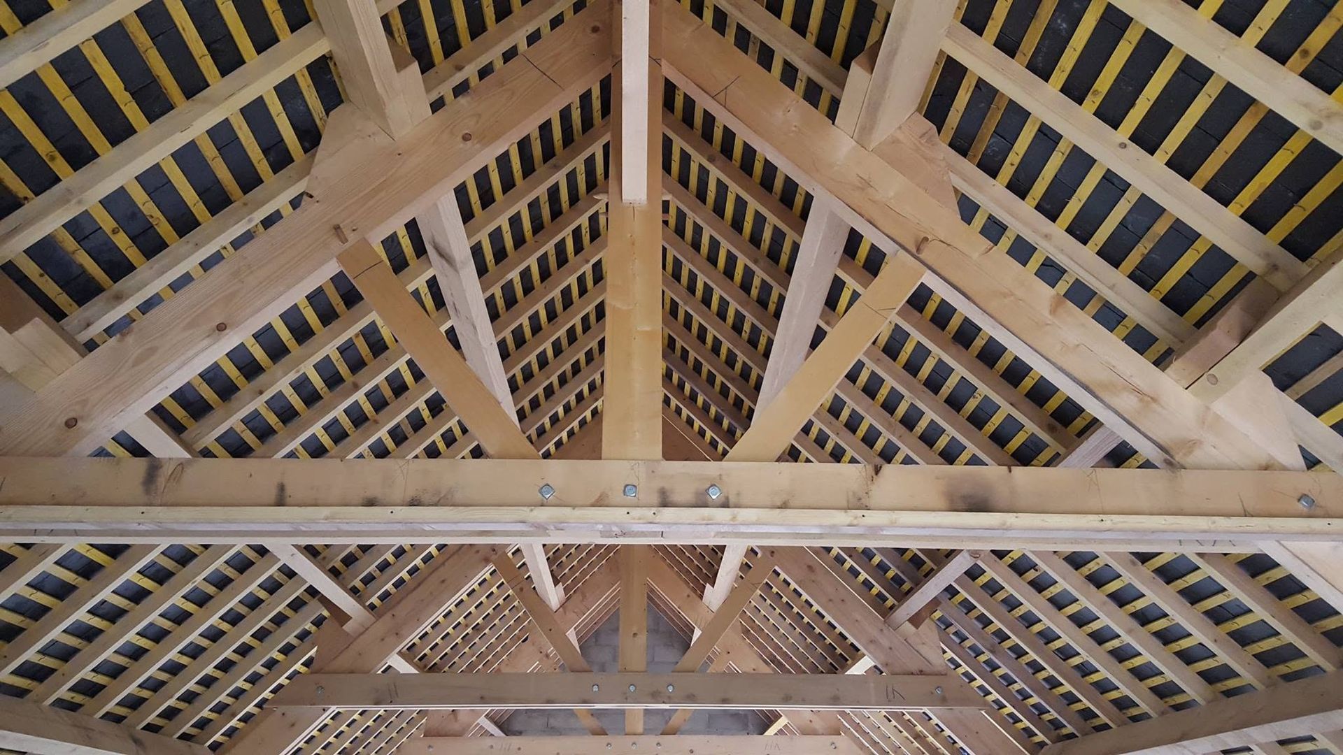 Charpente et poutres en bois vues d'en bas, avec puits de lumière et plafond clair.