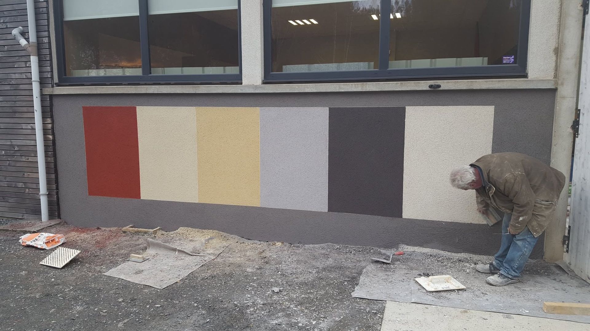 Un ouvrier peint un mur avec des échantillons de couleurs verticaux sous les fenêtres.