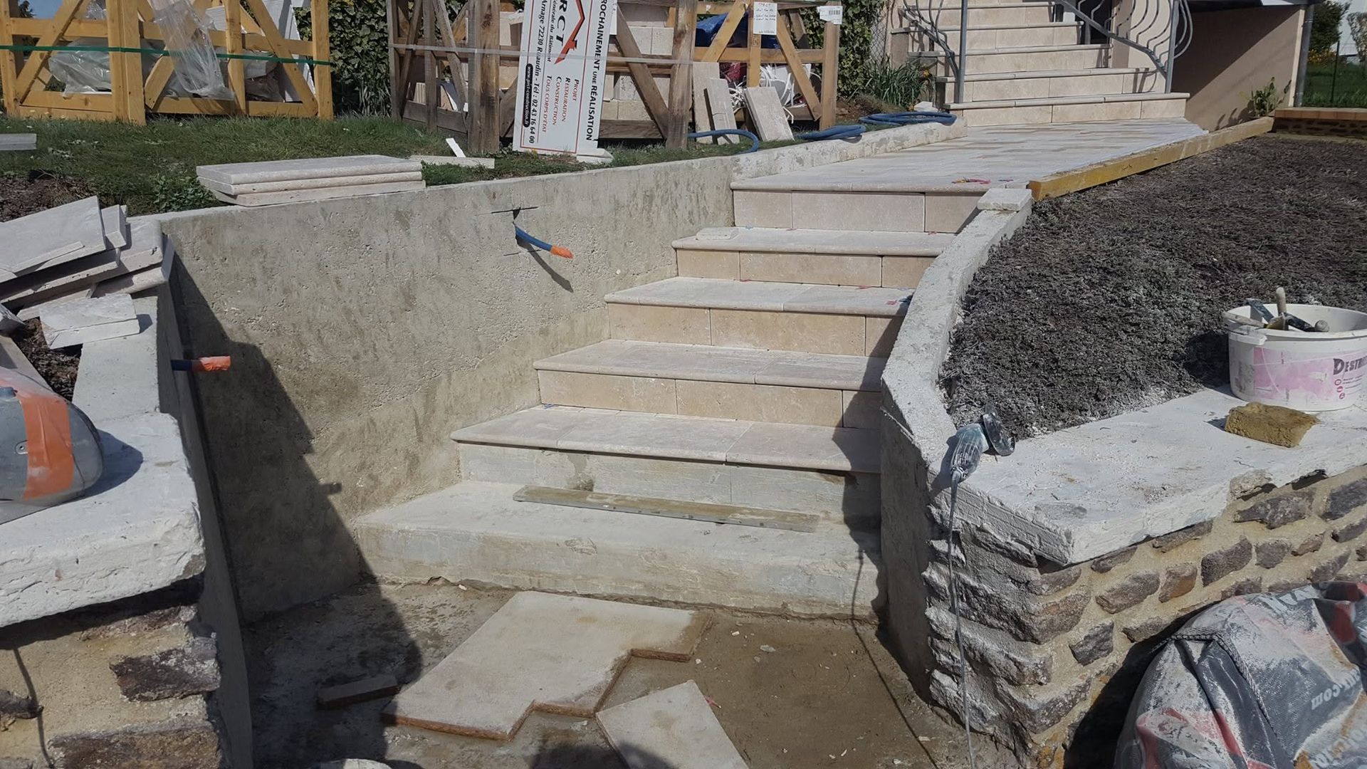 Escalier extérieur en pierre en construction à côté de murs de soutènement et d'aménagements paysagers en gravier.