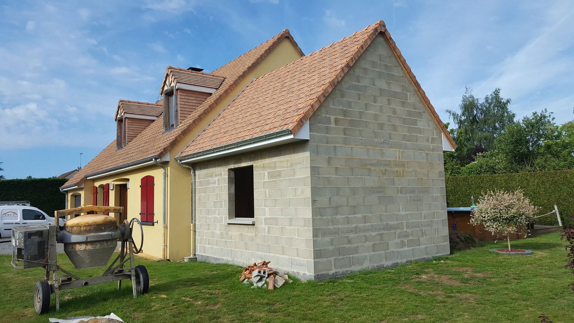 Maison neuve couleur crème avec toit de tuiles rouges et petite pelouse par une journée ensoleillée.