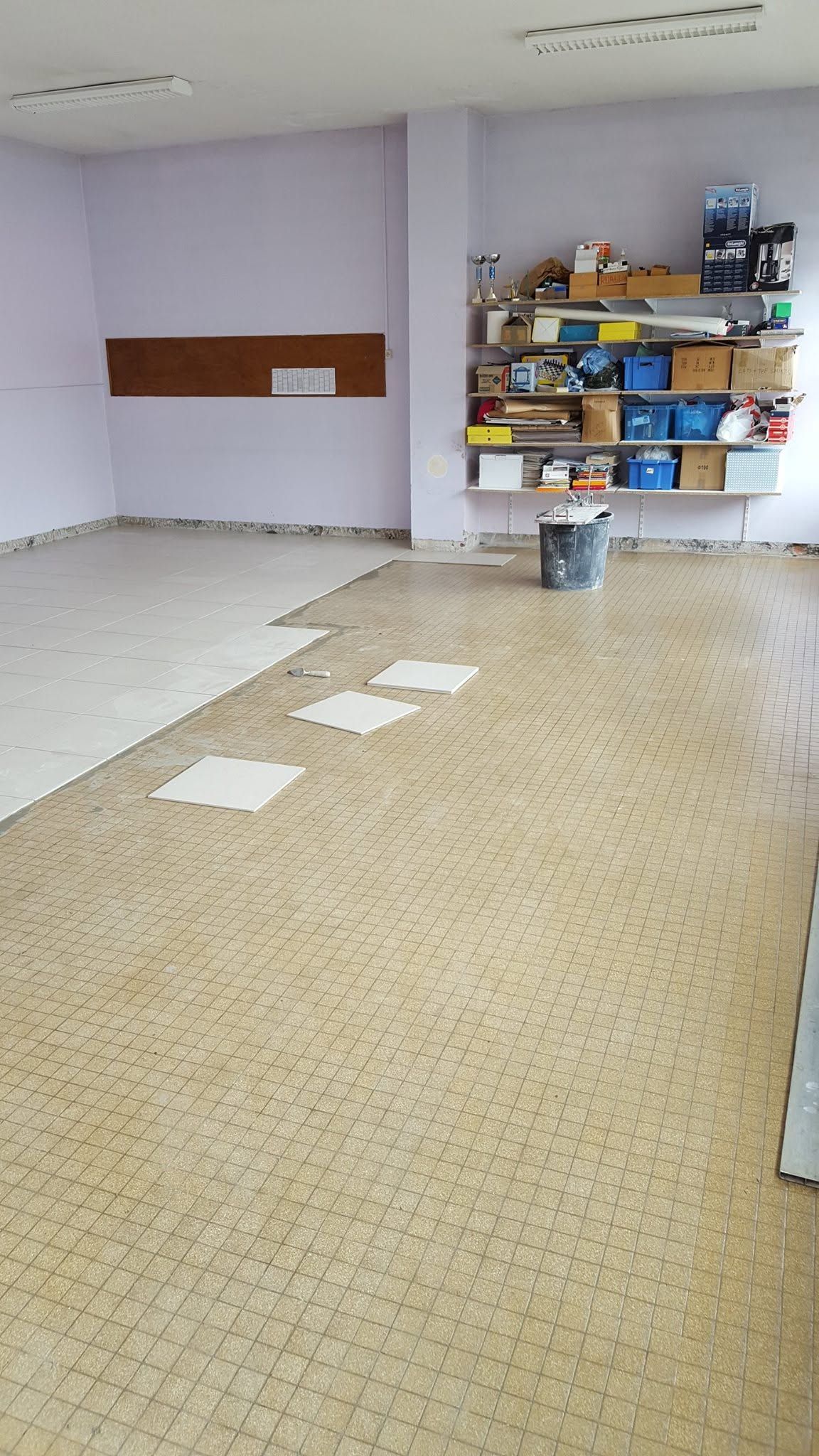 Pièce vide avec moquette beige, murs blancs, étagères murales et papiers éparpillés sur le sol.