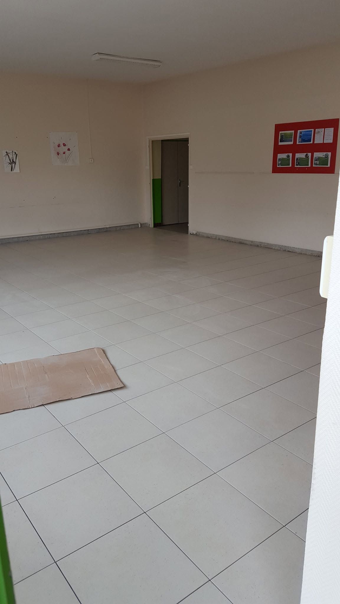 Pièce carrelée vide avec des murs beiges, une porte verte et un tableau d'affichage rouge.
