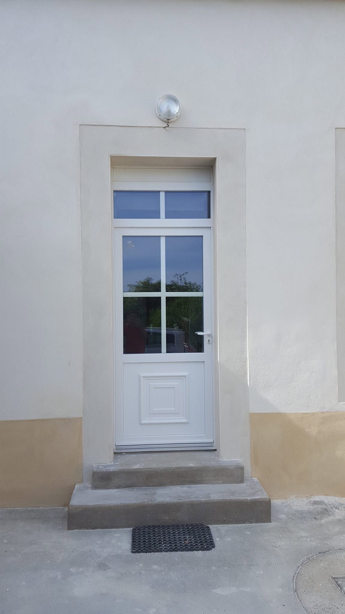 Porte blanche vitrée et petites marches dans une façade murale claire.