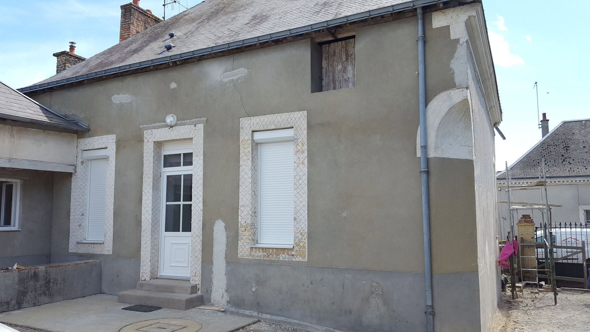 Petite maison grise avec des volets blancs et une porte d'entrée blanche sous un toit en pente.