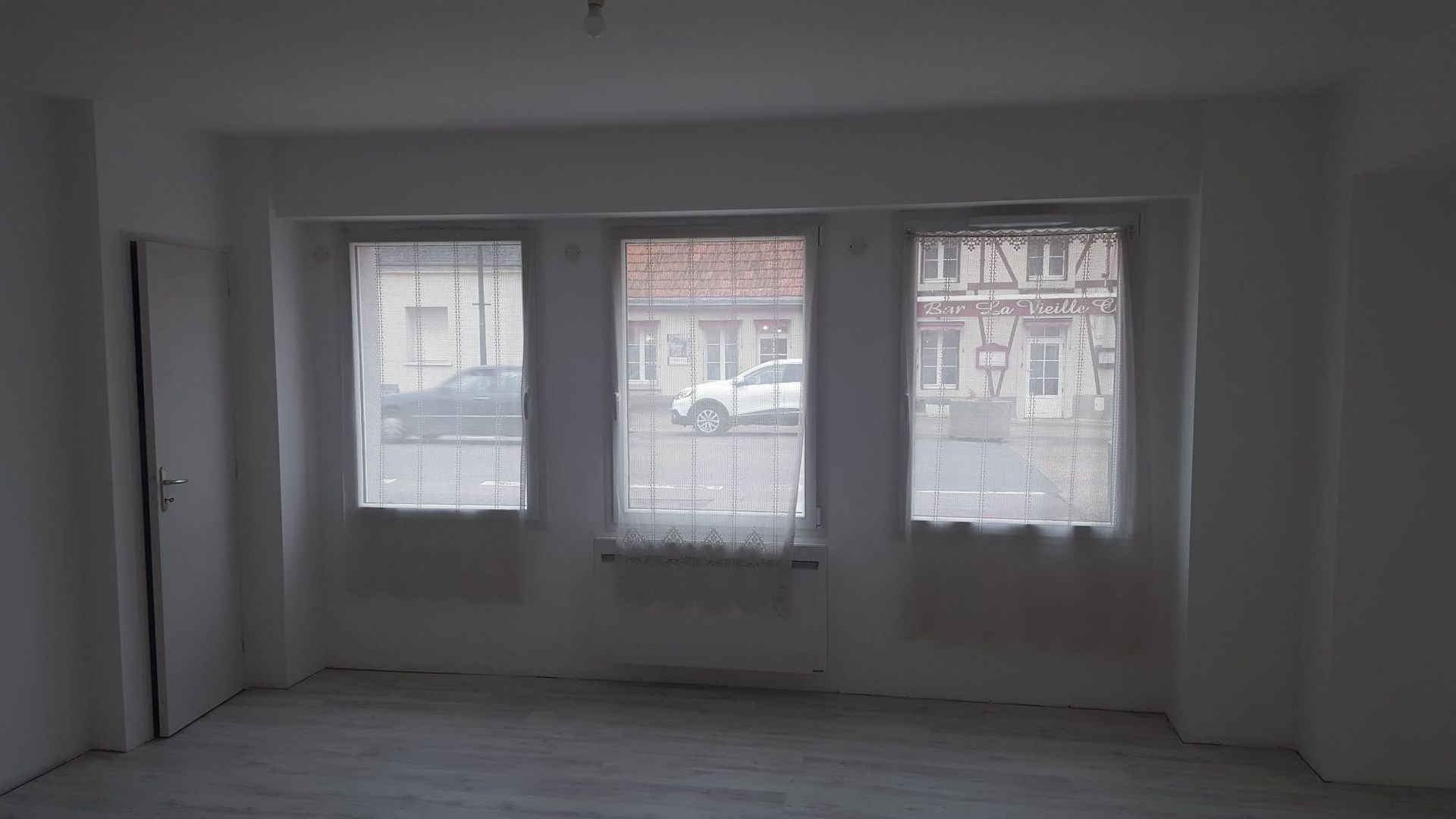 Pièce blanche vide avec trois fenêtres et un parquet clair, vue de l'intérieur.