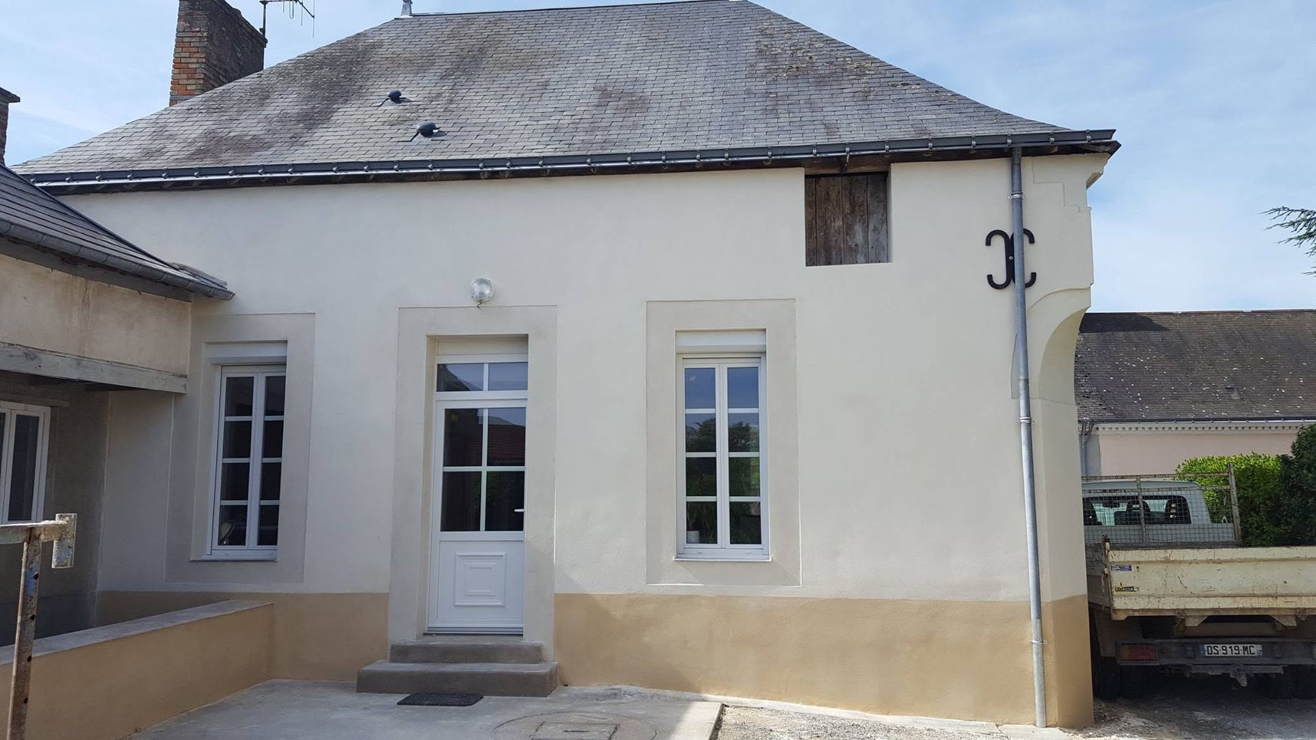 Petite maison blanche avec une porte d'entrée, des fenêtres et une façade inférieure beige clair.