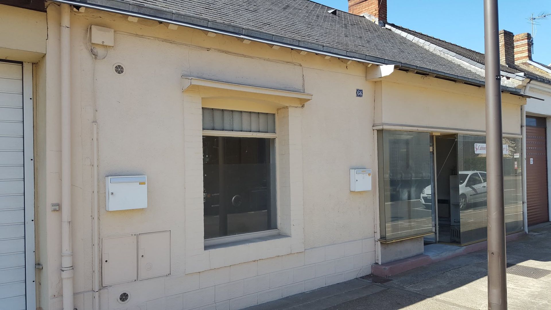 Petite boutique beige avec vitrine et porte vitrée donnant sur une rue ensoleillée.