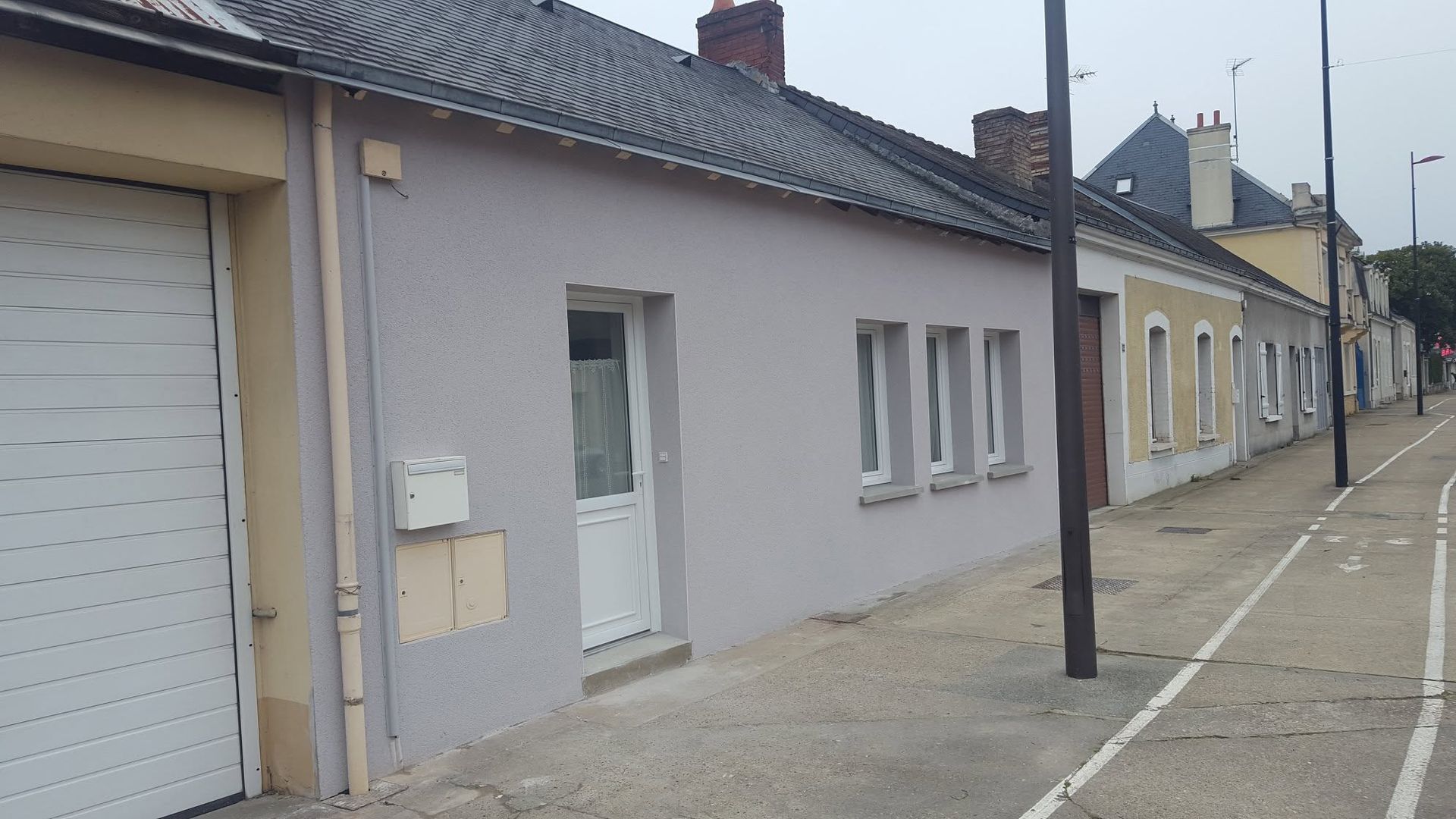 Rue tranquille bordée de maisons mitoyennes aux couleurs pastel, d'une porte de garage et d'un trottoir sous un ciel couvert.