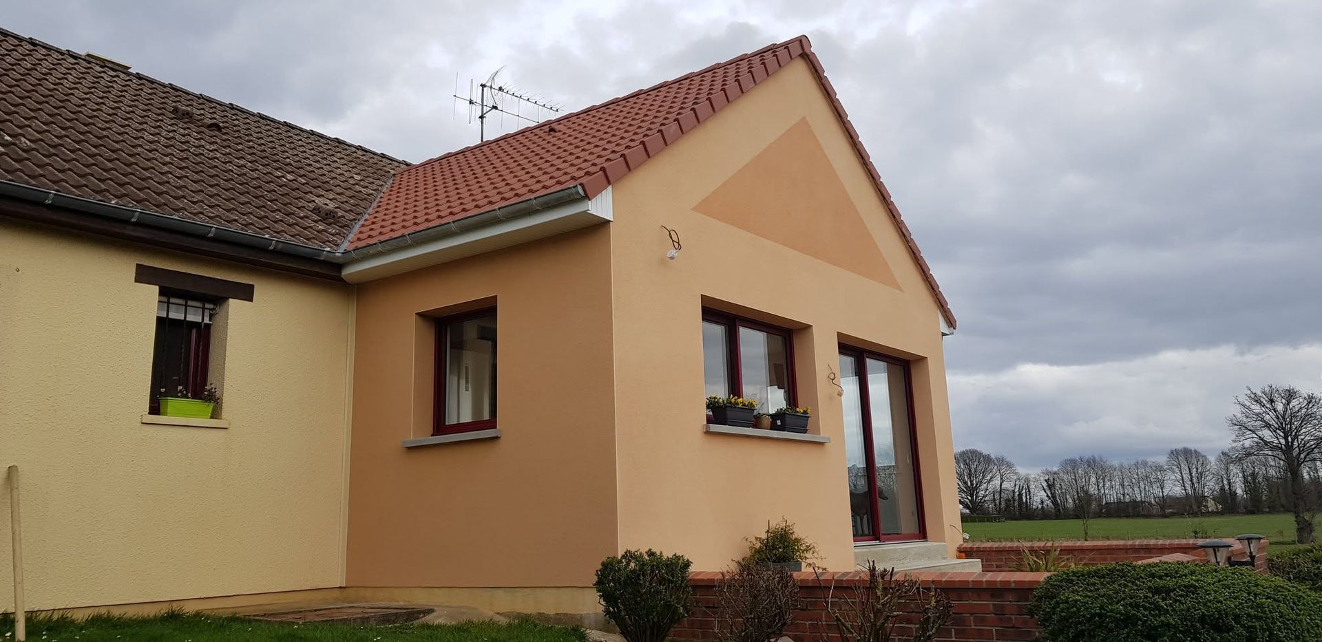 Maison couleur pêche avec toit de tuiles rouges et petite entrée principale dans un cadre rural.