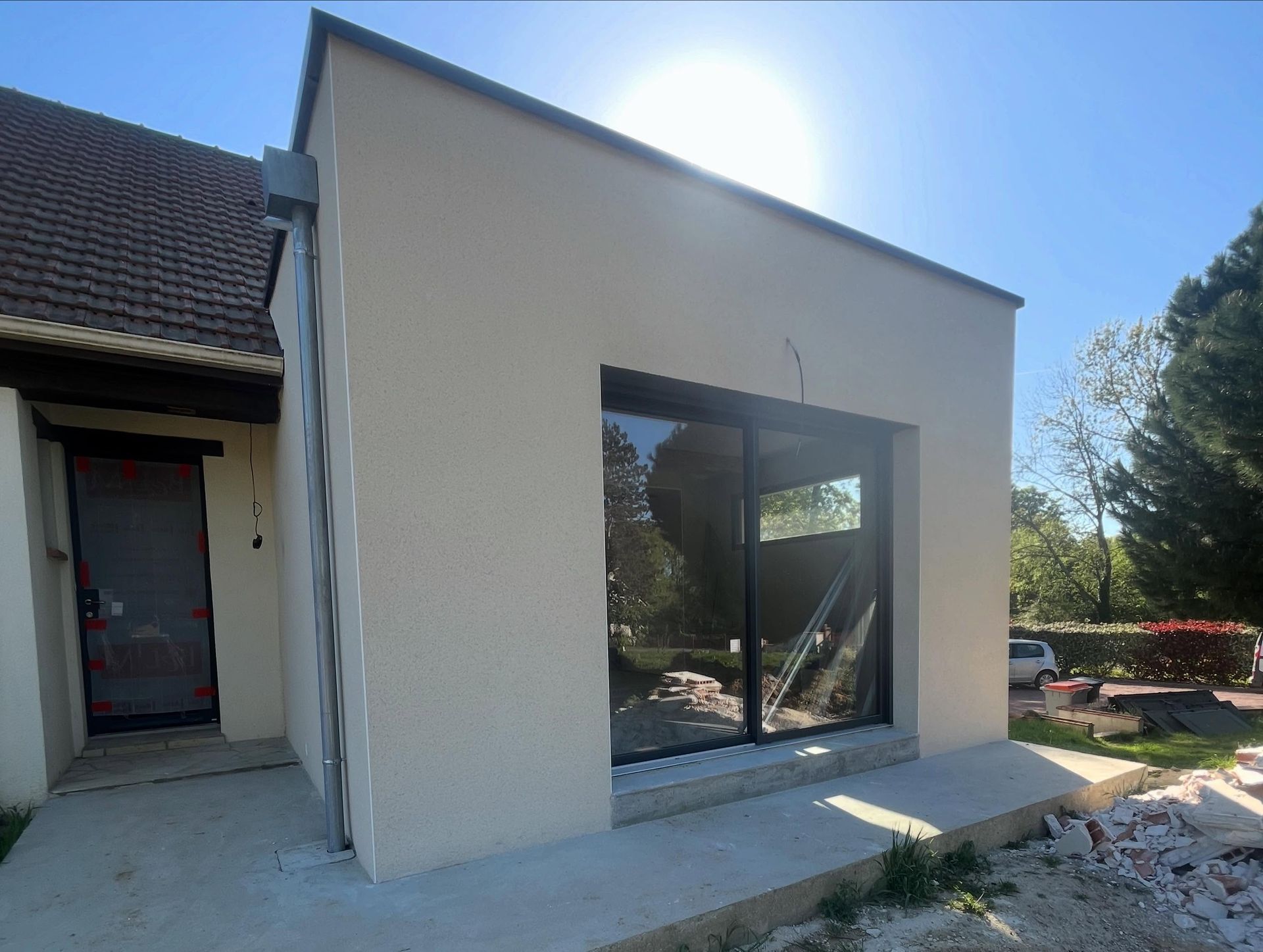 Extérieur d'une maison moderne avec une grande ouverture murale inachevée et un patio ensoleillé en construction.