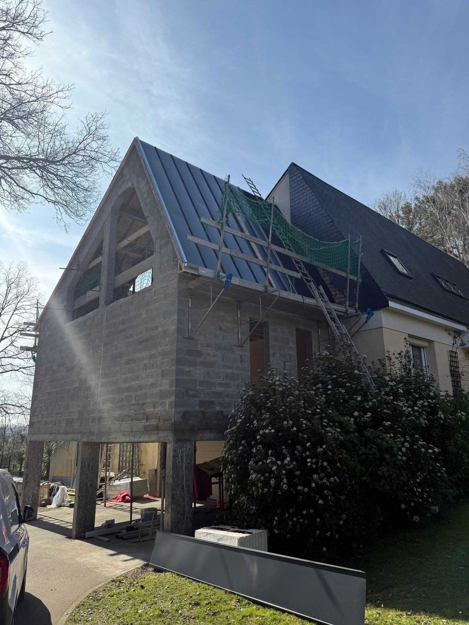 Maison partiellement construite avec toit en pente et échafaudages sous un ciel bleu.