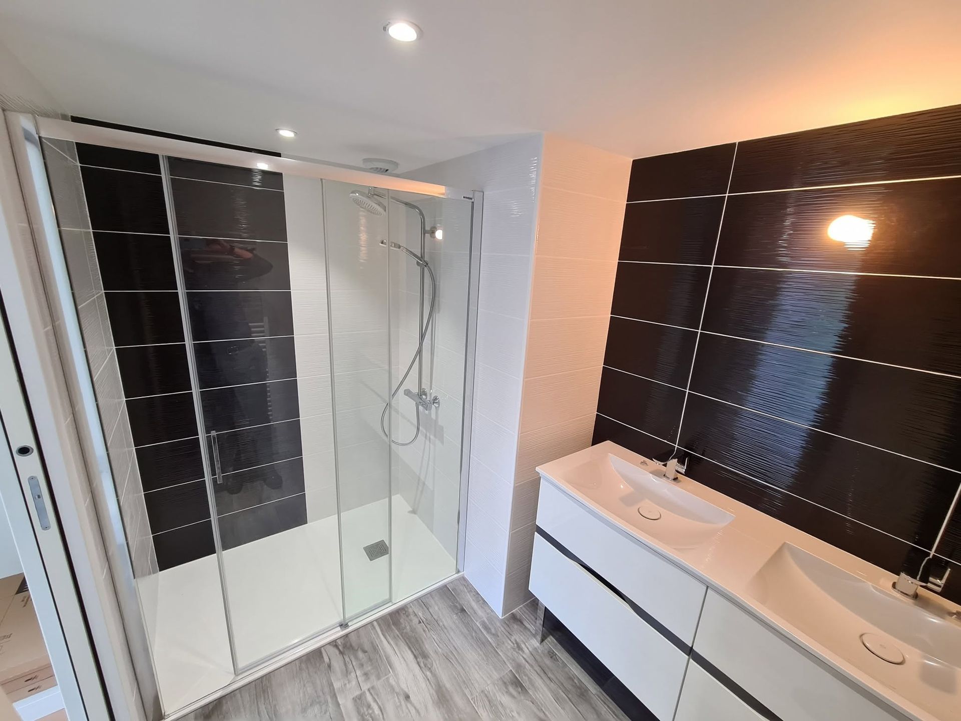 Salle de bains moderne avec douche à l'italienne, double vasque et murs carrelés noirs.
