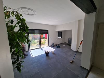 Salon vide avec sol carrelé foncé, grandes portes coulissantes et produits de nettoyage près du mur.