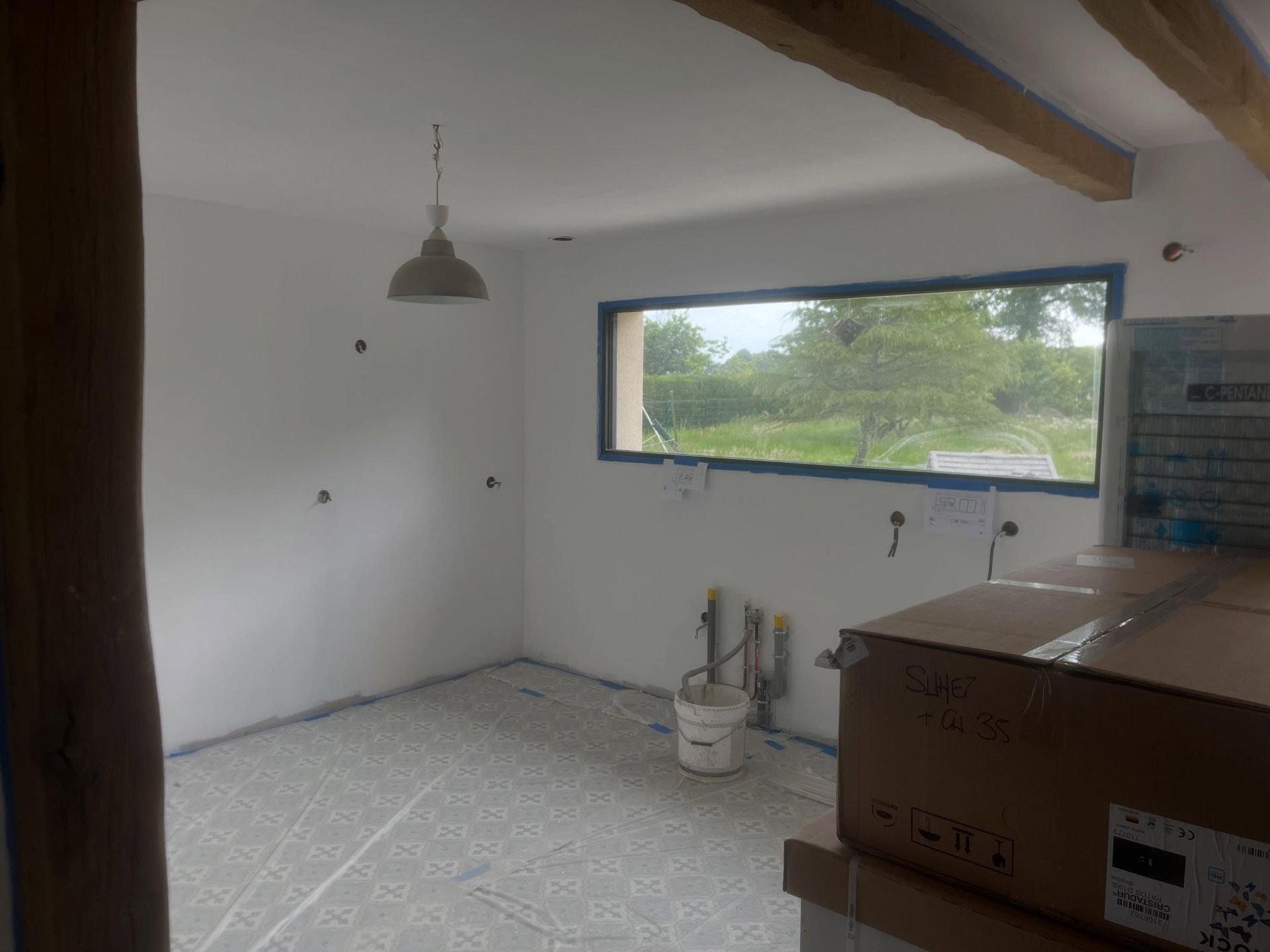 Cuisine inachevée avec murs blancs, fenêtre, suspension lumineuse et plan de travail au premier plan.