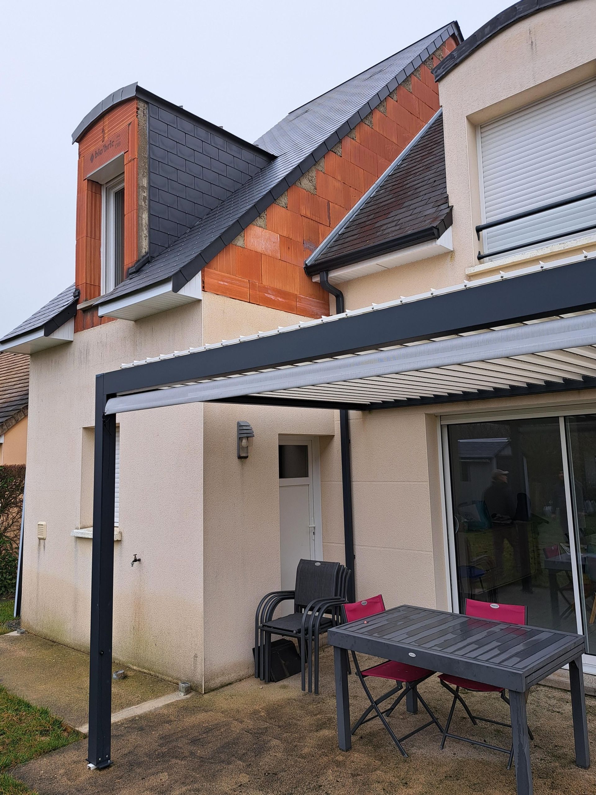 Terrasse moderne avec table, chaises et store rétractable sous un toit en pente.