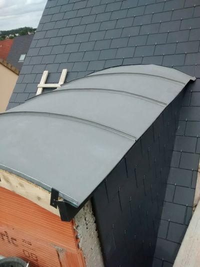 Auvent de toit gris incurvé, fixé au mur d'une maison en ardoise sombre, vu du dessus.