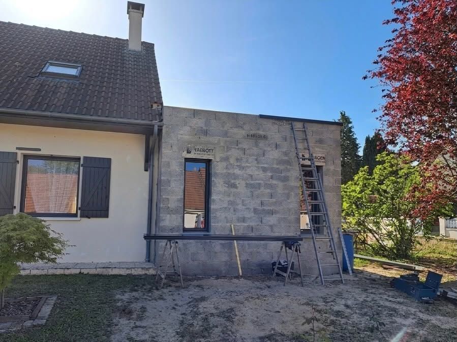 Extérieur de maison avec mur en pierre rénové, échelle et outils éparpillés sous un ciel bleu.