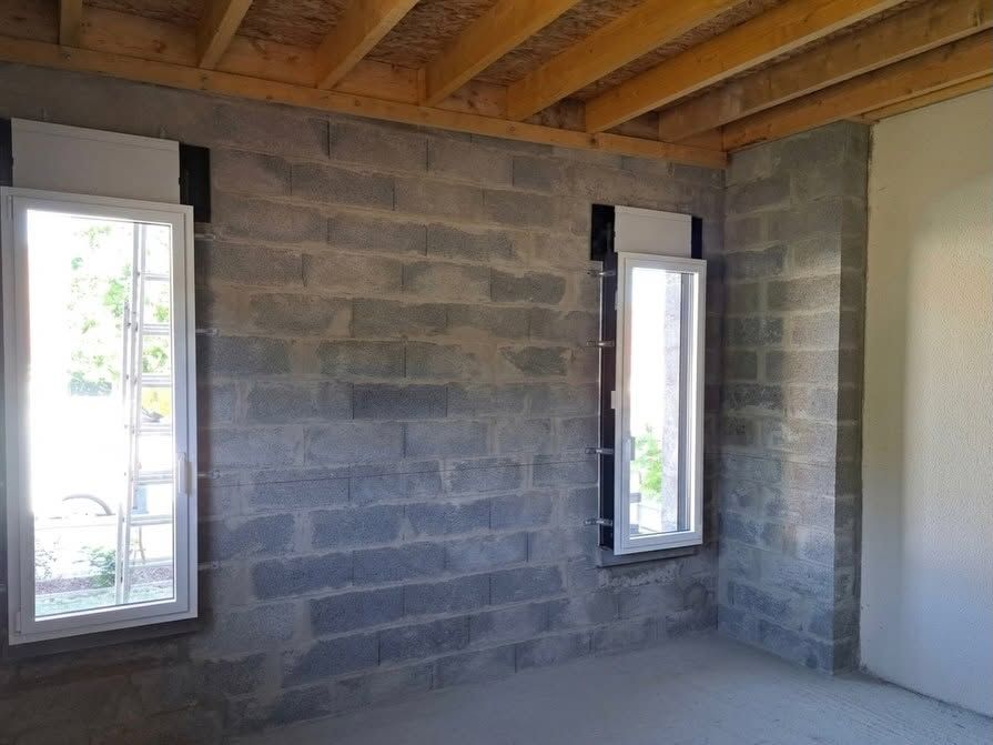 Pièce vide et inachevée, aux murs en parpaings, aux solives apparentes et dotée de deux fenêtres étroites.